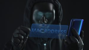 Hacker wearing black mask pulls MAC ADDRESS tab from a smartphone. Hacking concept